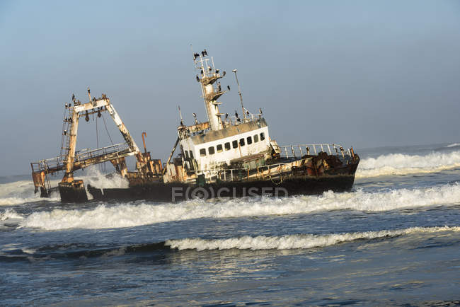 Un barco abandonado hundido oxidado en las olas - foto de stock