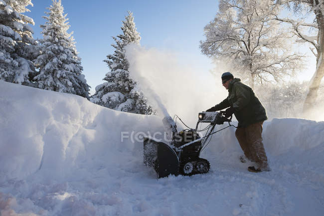 Un hombre usa un soplador de nieve en la nieve profunda; Homer, Alaska, Estados Unidos de América - foto de stock