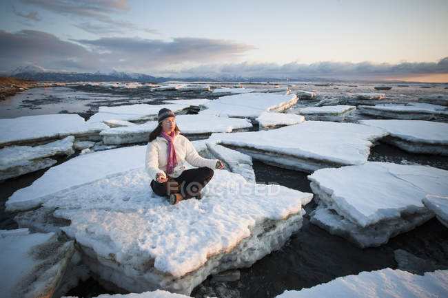 Mulher praticando meditação em pedaços de gelo empilhados contra o Homer Spit, Alasca — Fotografia de Stock