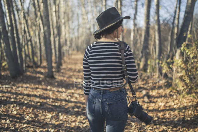 Young woman wearing hat with camera and walking through the woods near Creamer's Field, Fairbanks, Interior Alaska, Autumn — Stock Photo