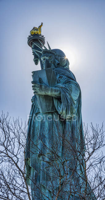 Sol brillando detrás de la antorcha de la Estatua de la Libertad - foto de stock