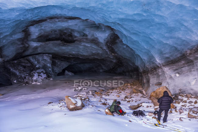 Dos hombres empacando su equipo después de explorar una cueva de hielo del glaciar Augustana en invierno. Alaska, Estados Unidos de América - foto de stock