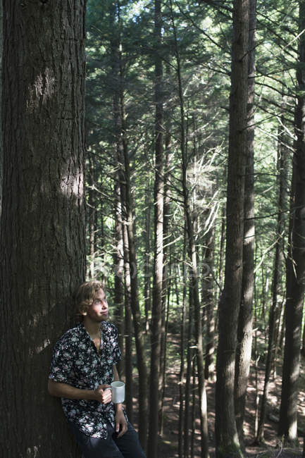 Jeune homme debout dans une forêt avec une tasse de café, Little River State Park ; Waterbury, Vermont, États-Unis d'Amérique — Photo de stock