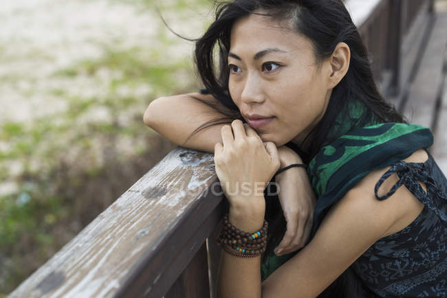 Young woman sitting against wooden railing and looking out at ocean — Stock Photo