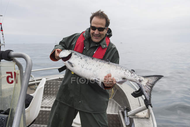 Hombre está parado en barco de pescado sosteniendo un salmón chinook grande recién capturado. Islas Queen Charlotte, Columbia Británica, Canadá - foto de stock