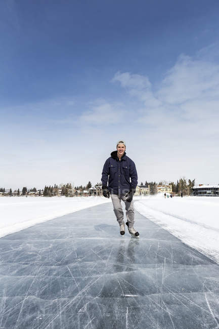 Pattinaggio dell'uomo sul ghiaccio appena curato sul lago con case sullo sfondo e cielo blu; Calgary, Alberta, Canada — Foto stock
