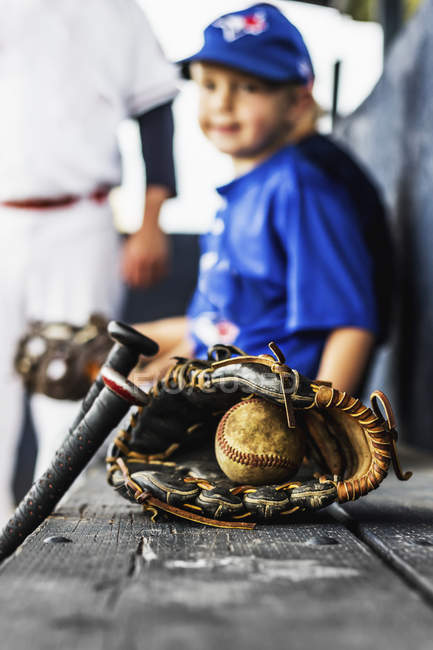 Two ball players in uniform sit in the dugout with their glove and baseball in focus in the foreground; Fort McMurray, Alberta, Canada — Stock Photo