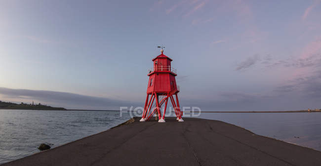 Red lighthouse along coast at sunset — Stock Photo