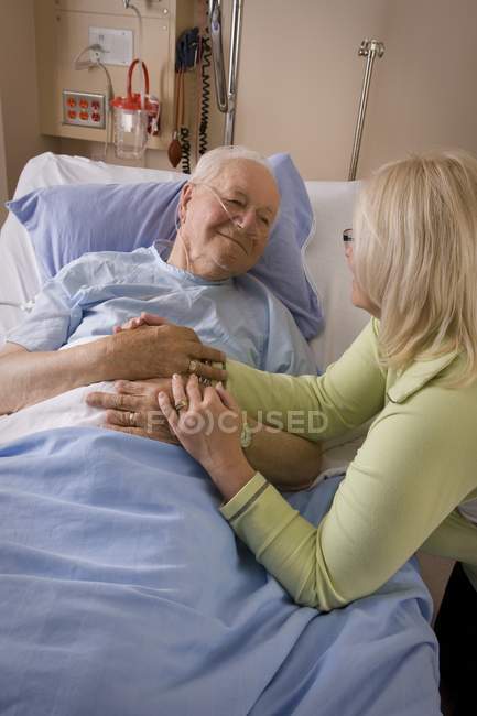 El anciano y su hija. Mujer sentada por hombre en cama de hospital - foto de stock