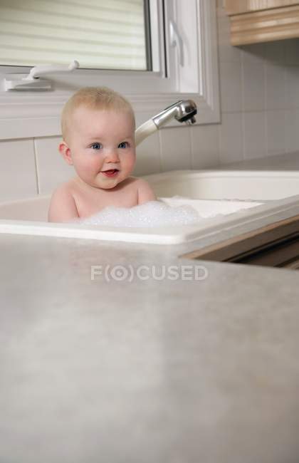 Happy adorable baby in kitchen sink — Stock Photo