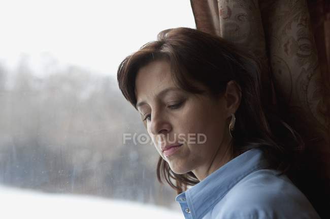 Frau lehnt mit geschlossenen Augen am Fenster — Stockfoto