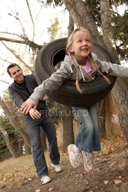 Padre spingendo figlia su pneumatico swing — Foto stock