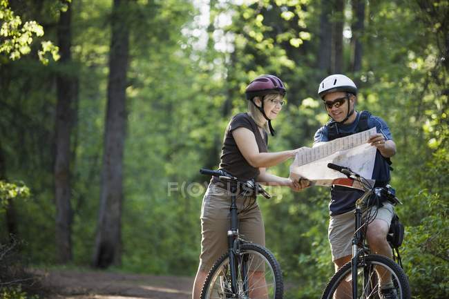Pareja caucásica en bicicletas mirando el mapa en la naturaleza - foto de stock
