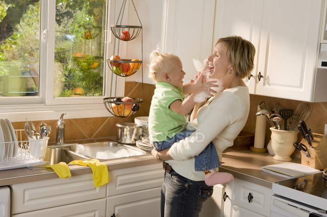 Caucasiano mãe e bebê filha abraçando na cozinha e se divertindo — Fotografia de Stock