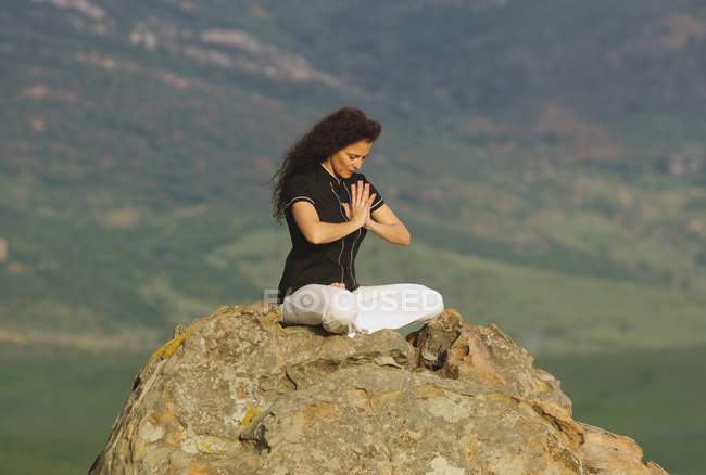 Woman meditating on top of boulder under sky — Stock Photo