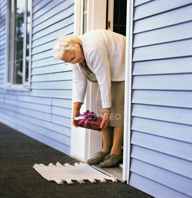 Пожилая женщина подбирает подарок из своей парадной двери — стоковое фото