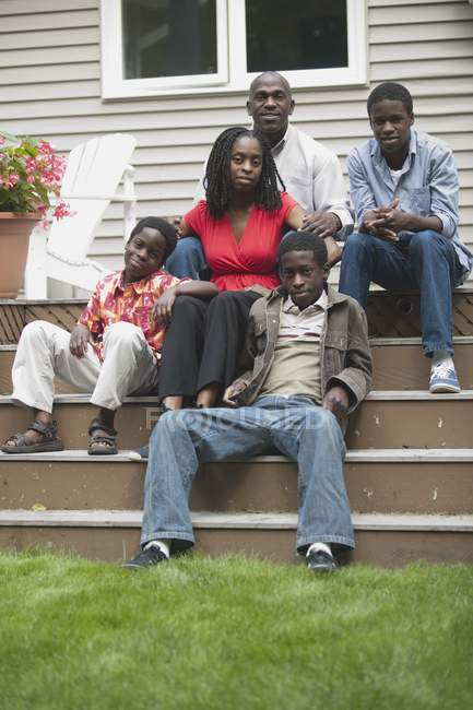 Портрет счастливой африканской американской семьи, сидящей на лестнице своего дома и смотрящей в камеру — стоковое фото