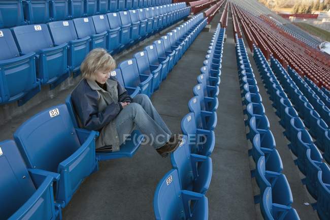 Mature caucasian woman sitting alone in empty stadium — Stock Photo
