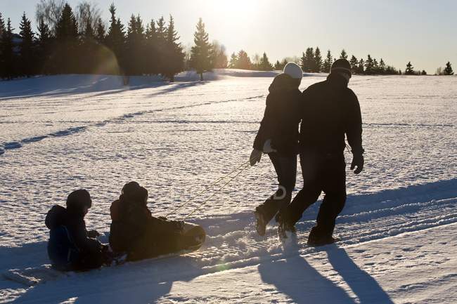 Счастливая Кавказская семья, родители, несущие сани с детьми на зимнем снегу — стоковое фото