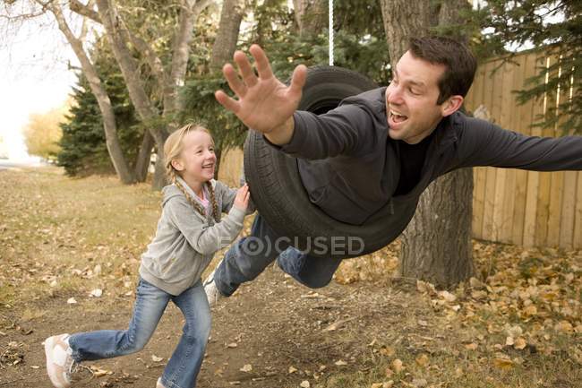 Figlia spingendo padre su pneumatico swing — Foto stock