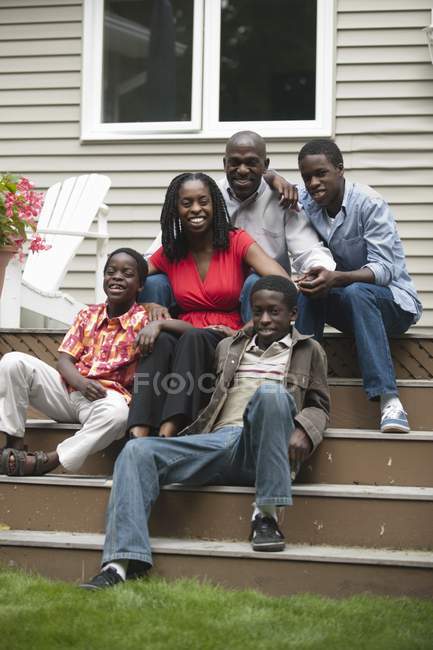 Portrait of happy african american family sitting on stairs of their home and looking at camera — Stock Photo