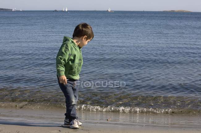 Niño de pie en la playa contra el agua ondulada - foto de stock