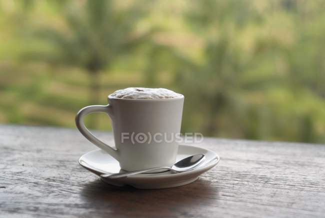 Xícara branca de café com espuma na placa com colher closeup — Fotografia de Stock