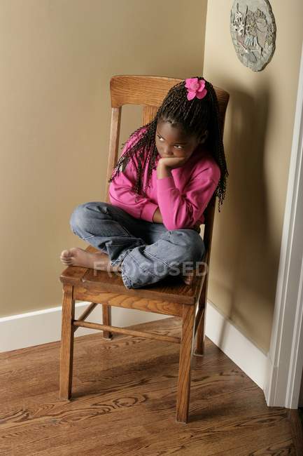 Triste fille assis sur la chaise dans le coin — Photo de stock