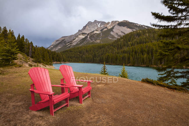 Deux chaises Red Adirondack sur une colline herbeuse dans les montagnes et les lacs de l'Alberta ; Alberta, Canada — Photo de stock