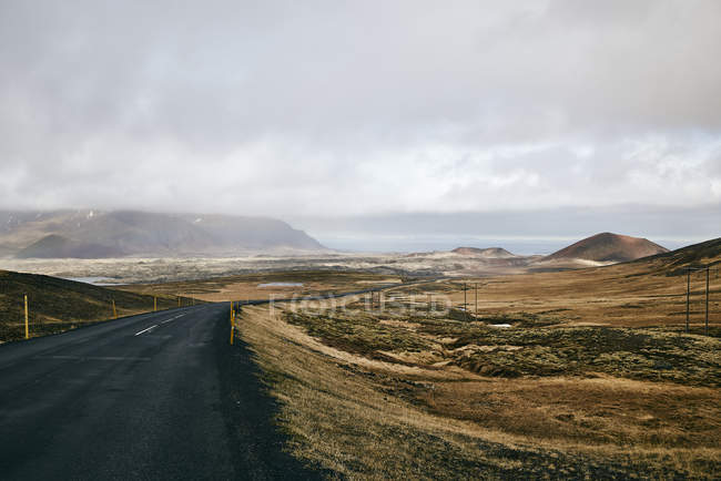 Una strada asfaltata lungo la costa sotto un cielo nuvoloso; Islanda — Foto stock