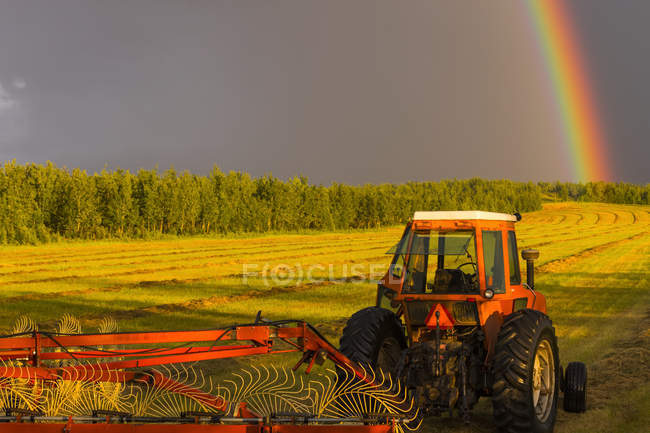 Vista del trattore che lavora sul campo con strumento e arcobaleno sopra la foresta sullo sfondo — Foto stock