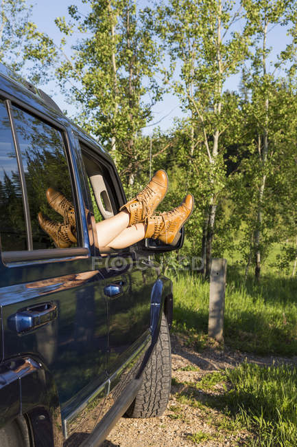 Vista delle gambe delle donne in stivali sul bordo della finestra auto contro gli alberi — Foto stock