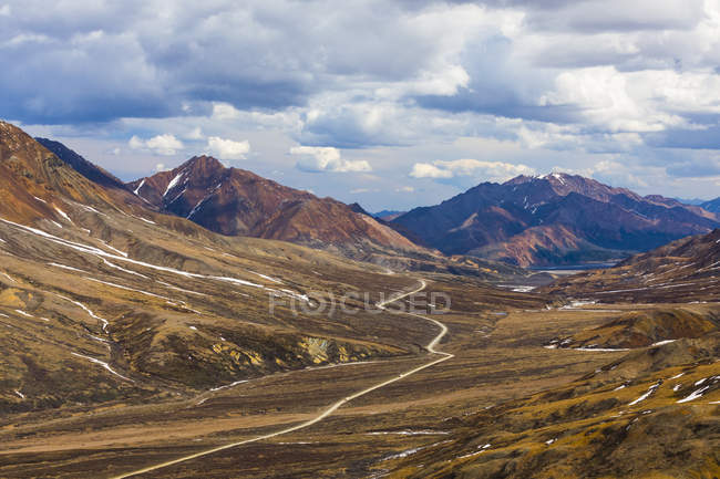 Vista del valle de la montaña con el río arroyo de agua y picos bajo el cielo nublado - foto de stock