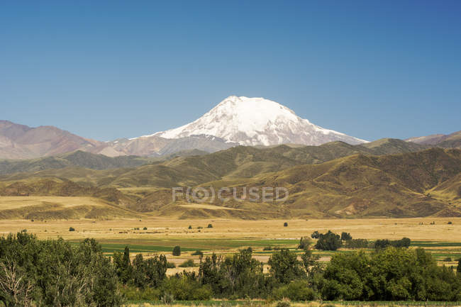 Volcán cubierto de nieve se eleva sobre las estribaciones de los Andes y las tierras de cultivo; Mendoza, Argentina - foto de stock