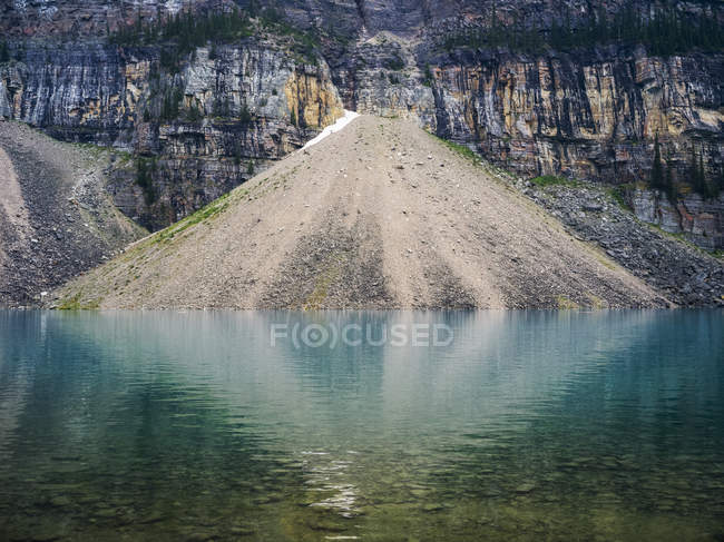 Pendiente del acantilado rocoso con arena contra el agua azul clara - foto de stock