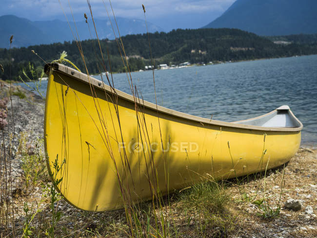 Желтая деревянная лодка пришвартовалась на берегу у озера днем — стоковое фото