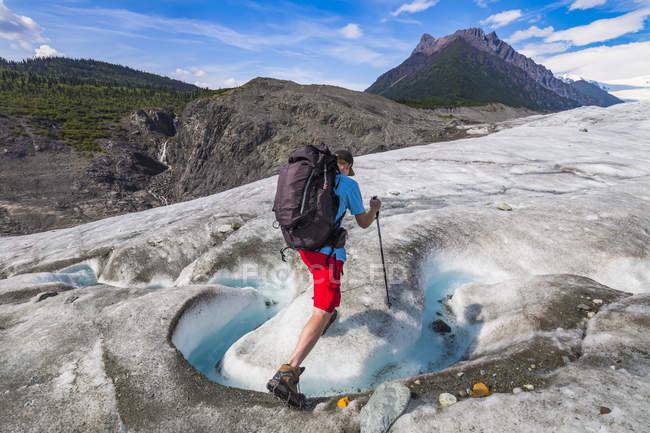 Mann in roten Shorts wandert in den Bergen mit Rucksack und Gipfeln im Hintergrund — Stockfoto