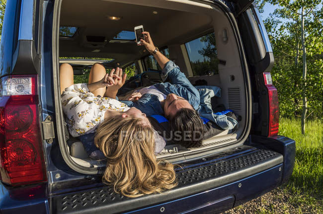 Jovem casal deitado no carro e olhando para o smartphone durante o dia — Fotografia de Stock