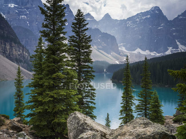 Limpida acqua blu del lago di montagna e alberi sulla riva con cime innevate sullo sfondo — Foto stock