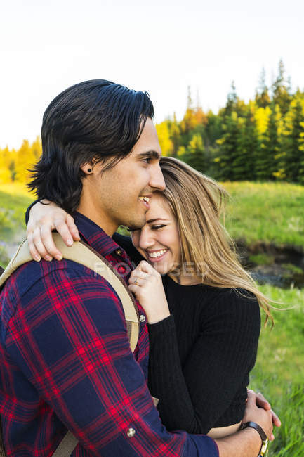 Jovem casal romântico em pé no campo e abraçando uns aos outros com árvores no fundo — Fotografia de Stock