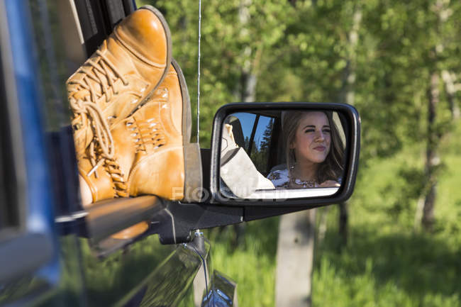 View of womans legs in boots on cars window edge and reflection in mirror against trees — Stock Photo