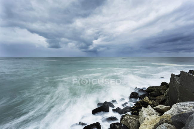 Скелі і камені проти хвилястої води під хмарним небом вдень — стокове фото
