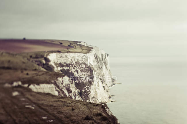 Cliff rochoso com grama sobre a água do mar durante o dia — Fotografia de Stock