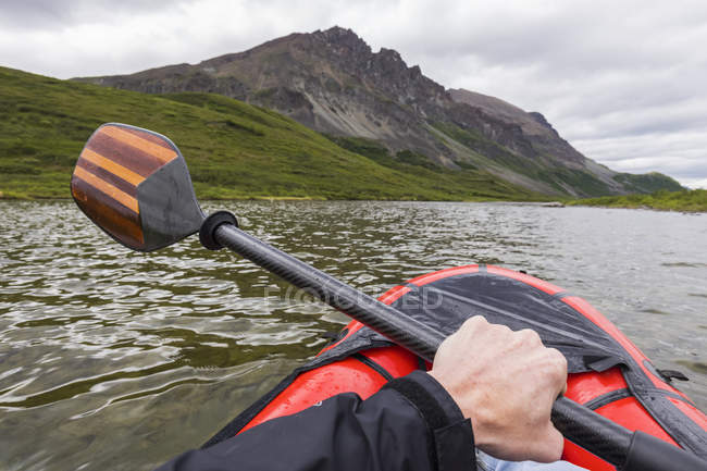 Paddle in hand over boat in river water with hills on shore — Stock Photo