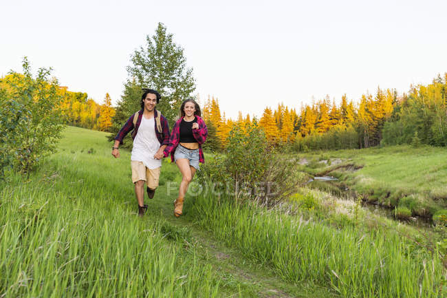 Pareja feliz corriendo sobre hierba verde al aire libre durante el día con la mano en la mano - foto de stock