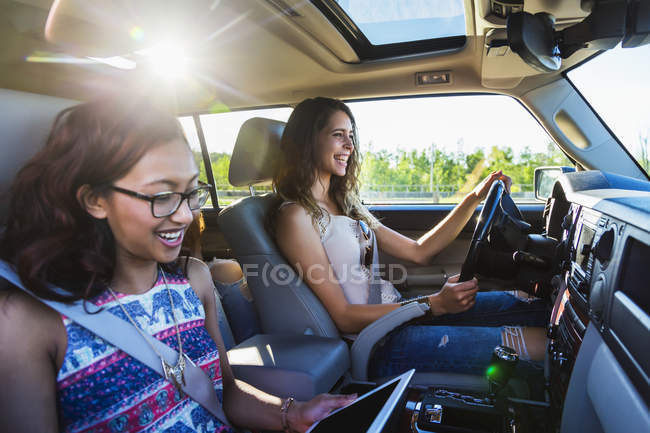 Two girls sitting in car while one driving another one looking at digital tablet — Stock Photo