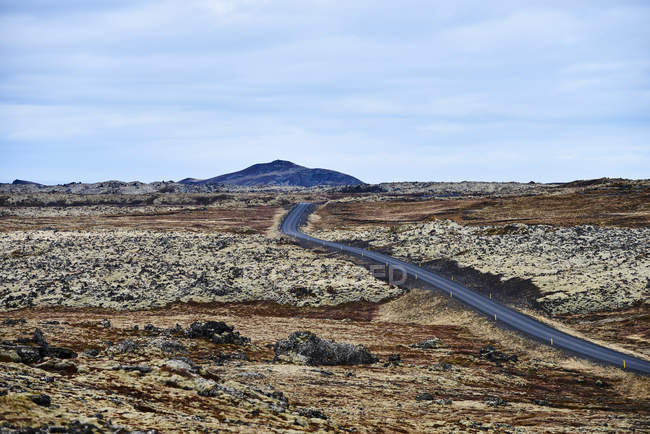 Un'autostrada corre attraverso un paesaggio arido con una montagna in lontananza, penisola di Snaefellsnes; Islanda — Foto stock