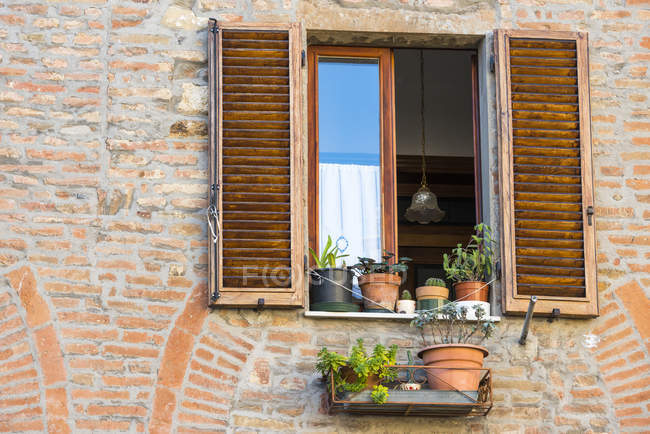 Chiudi Veduta di una facciata in mattoni di Montepulciano con finestra aperta, vasi da fiori e tende da sole merlate; Toscana, Italia — Foto stock
