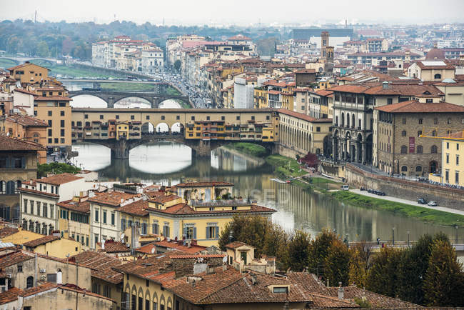Vista de edificios, techos coloridos, puentes antiguos (Ponte Vecchio) y flexión del río Arno; Florencia, Toscana, Italia - foto de stock