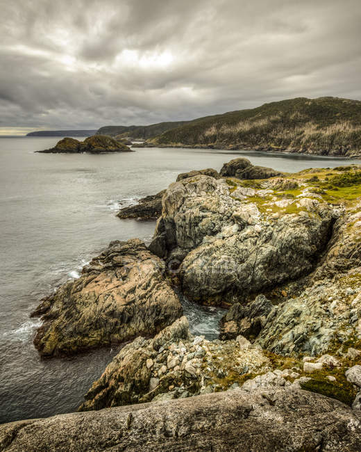 Large rock boulders over sea water and hills on background under cloudy sky — Stock Photo
